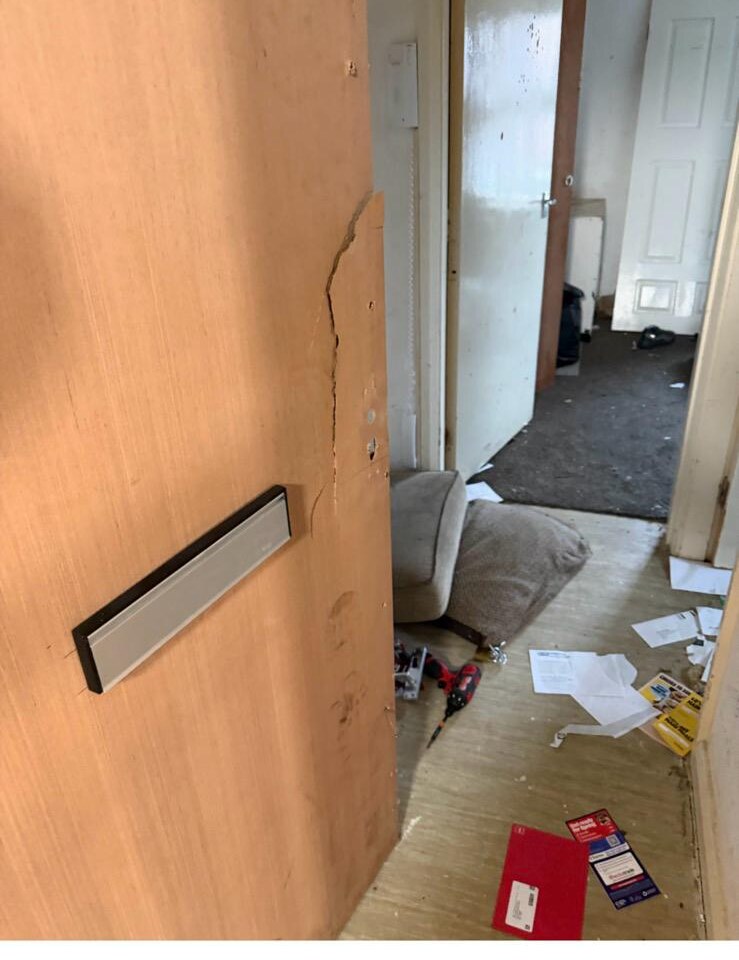 Interior view of damaged front door and frame with debris on the floor after a police entry call-out